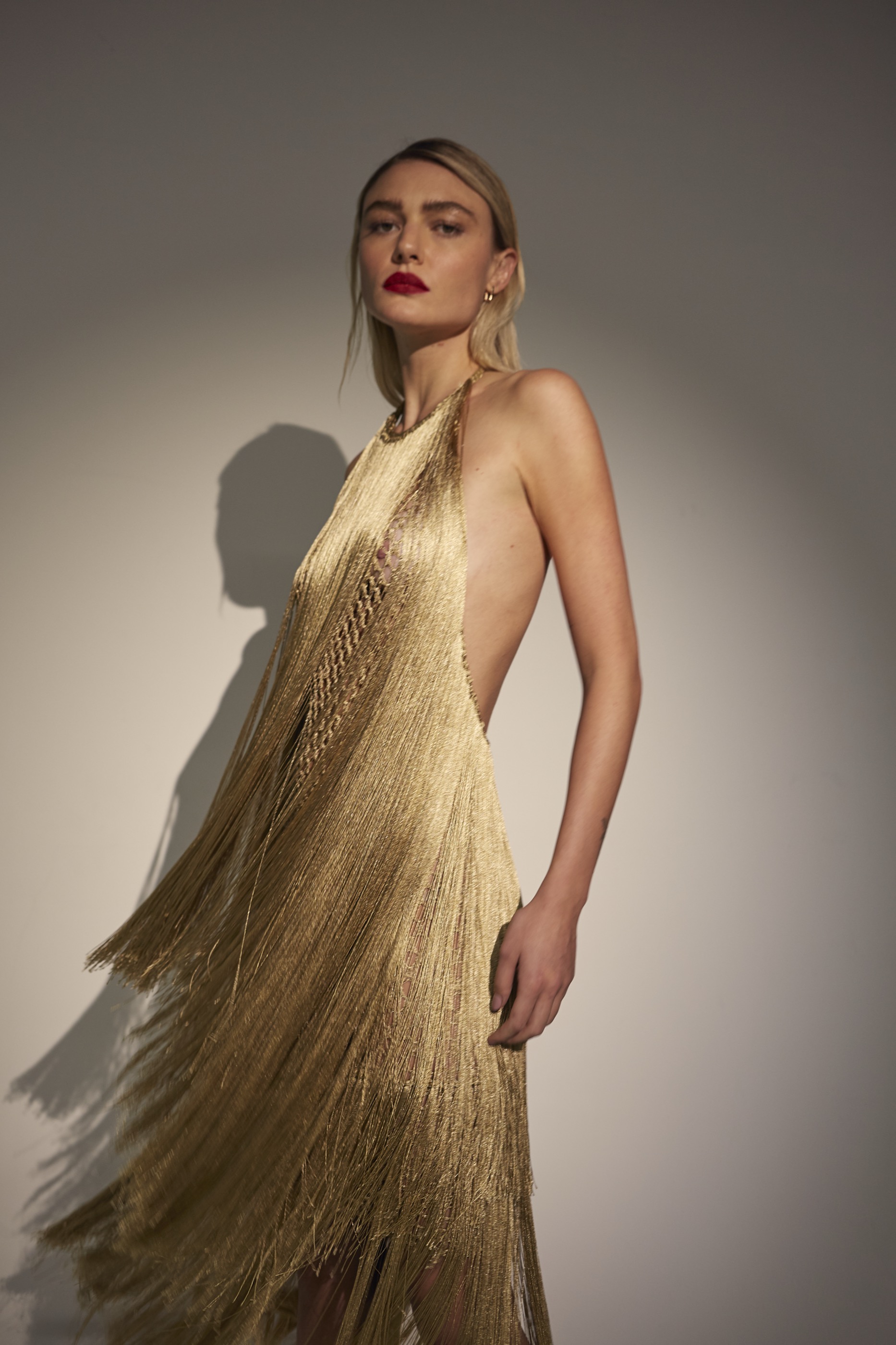 Blonde model wearing a long gold fringed dress